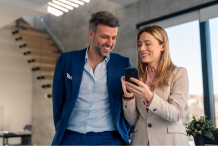 A business man and woman walking together looking at cell phone and smiling