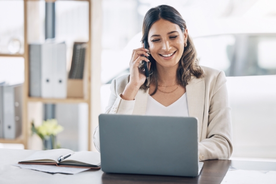 Smiling business woman talking on the phone and using laptop
